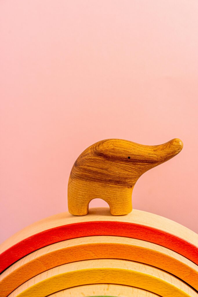 Charming wooden elephant toy on a colorful rainbow arch against a soft pink background.